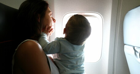 Baby reaching out to plane window. Mother traveling with infant son child