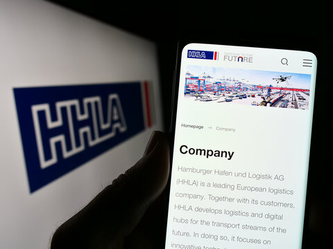 Stuttgart, Germany - 04-20-2023: Person holding smartphone with webpage of company Hamburger Hafen und Logistik AG (HHLA) on screen with logo. Focus on center of phone display.
