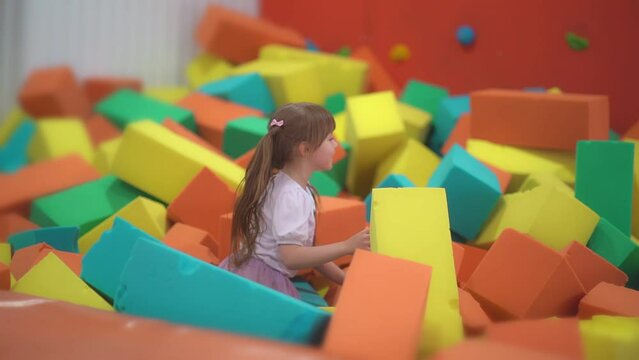 Little happy girl play and have fun in a dry pool with soft multicolored cubes in a children's entertainment center and throw paralon block in the playroom.