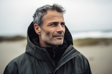 Handsome middle-aged man with grey hair and beard looking away at the beach