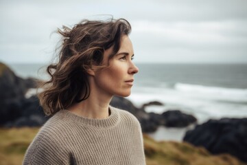Photography in the style of pensive portraiture of a pleased woman in her 30s wearing a cozy sweater against a summer landscape or beach background. Generative AI