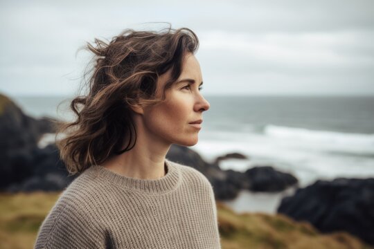 Photography in the style of pensive portraiture of a pleased woman in her 30s wearing a cozy sweater against a summer landscape or beach background. Generative AI