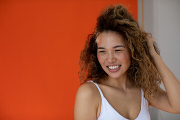 Smiling woman with curly hair and freckles on her face on orange background.