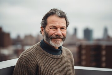 Portrait of a handsome senior man with grey hair, wearing a woolen sweater, standing on a balcony overlooking the city.