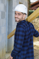 smiling carpenter holding wood planks in a construction site