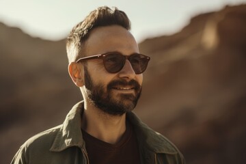 Portrait of handsome young man with beard in sunglasses looking away while standing outdoors