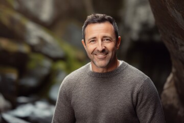 Portrait of a handsome mature man smiling at the camera while leaning against a rock