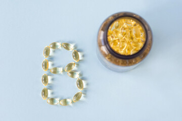 The transparent capsules are on the surface in the form of the letter B next to the can with vitamins on a blue background.