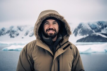 Fototapeta na wymiar Handsome man in warm jacket with hood standing in front of icebergs in Antarctica
