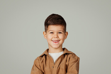 Cheerful cute european little child 6 years old in shirt looking at camera isolated on gray background