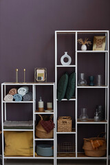 Rack of shelves with large variety of home supplies such as rolled towels, baskets, vases, cushions and picture frames standing by wall