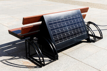 Solar panel bench. Charging phone while resting on a bench in city center. Smart solar bench. Modern technology invention. Inductive charger background.