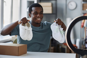 Happy young male shopaholic boasting with new gumshoes to online audience while unpacking ordered...
