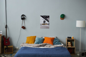 Part of spacious bedroom of teenager with comfortable double bed standing by grey wall with poster, cap and headphones