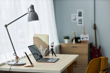 Lamp on desk with laptop which is workplace of student, designer or freelancer standing window with white chiffon curtains in bedroom