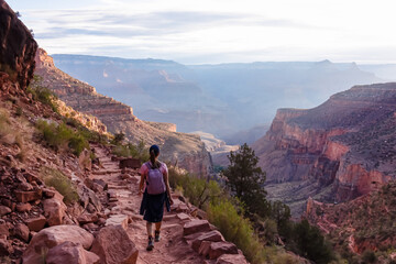 Rear view of woman with backpack hiking along Bright Angel trail with panoramic aerial overlook of...