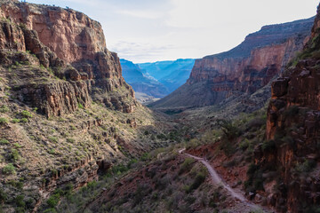 Fototapeta premium Panoramic aerial view from Bright Angel hiking trail at South Rim of Grand Canyon National Park, Arizona, USA. Vista after sunrise in summer. Colorado River weaving through valleys and rugged terrain