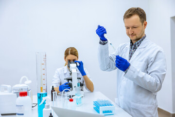 Male scientist analyzes liquid female researcherworking with microscope investigating medical sample