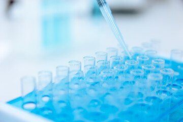Unrecognizable scientist dripping blue liquid from pipette into test tube at table in laboratory.