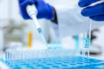 Unrecognizable scientist dripping blue liquid from pipette into test tube at table in laboratory.