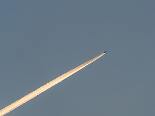 The plane flies in the blue sky and leaves a bright trail
