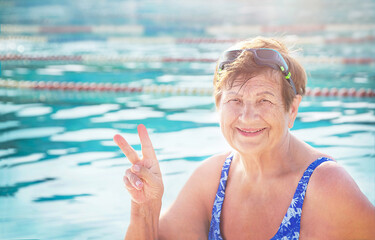 Active senior (elderly) woman (over age of 50) in swimsuit, sport goggles smiling and doing victory...
