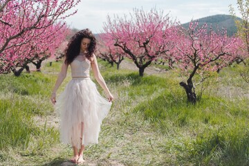 A young girl among beautiful peach flowers in full bloom. Pink peach blossom garden. Springtime.