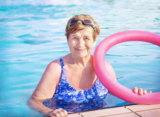 Active senior (elderly) woman (over age of 50) in sport goggles, swimsuit and with swim noodles in...