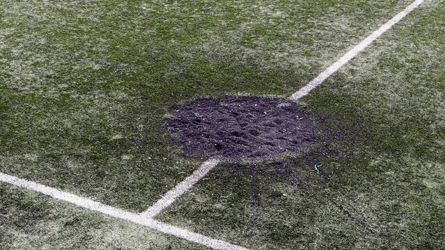 A hole in the ground from a cannon shell explosion filled with fresh earth at a football stadium. Shelling crater in the city. Playground. War in Ukraine. Destruction of civilian infrastructure.