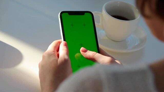 Girl scrolling phone green screen browsing social media chroma key reading news close up hands cup of coffee 