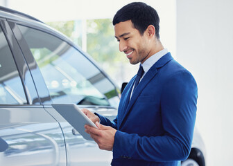 Looking through the dealership database. a handsome young male car salesman working on the showroom floor.