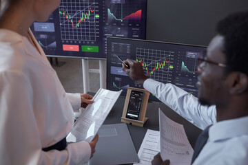 Businessman pointing at monitor with graphs and discussing the growth of stocks together with his colleague