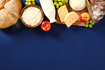 Fototapeta na wymiar Shavuot dairy food, grape, apples and cereal breads on blue background. Flat lay, top view.
