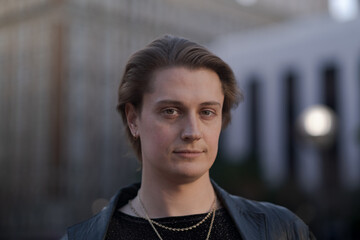 Fototapeta premium Against a background of tall buildings during warm golden hour light, a genderfluid model exudes confidence and style while, donning a black leather jacket.