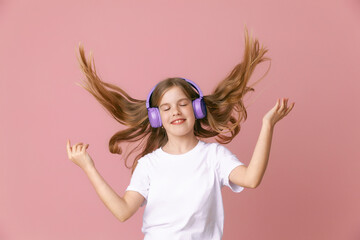 Photo of a cute funny young teenage girl in a pink jumper, headphones, dancing, enjoying music on a...