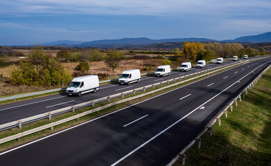 Eight white minivans are moving in a convoy on the highway. White delivery van on the highway....