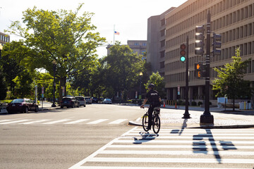 Washington, DC, USA - May, 2022: Police officer riding a bicycle and crossing crosswalk on avenue...