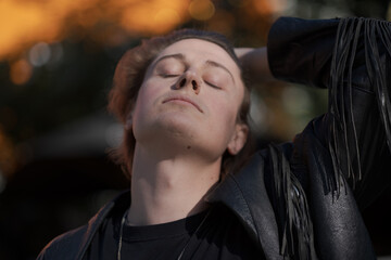 Embracing their unique identity, a genderfluid model confidently poses outside a tall building during golden hour, their black leather jacket adding an edgy touch to the casual yet captivating scene.