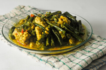 long bean vegetables and sliced tempeh with coconut milk sauce served on a small plate and a napkin isolated on a white background