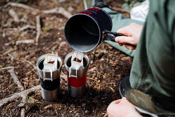 Cooking system on a camping trip, a guy pours boiling water into a glass, a thermo mug, brew a...