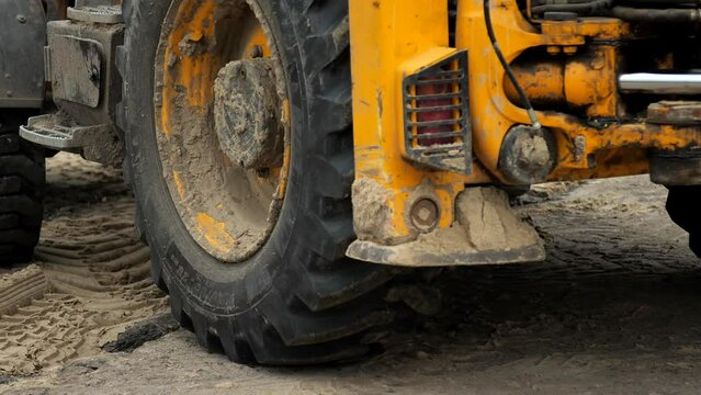 Tractor excavator rides in reverse during repair work at a construction site. Repair of communications in the city. The loader backs up. Close-up of the big wheels of a driving tractor.