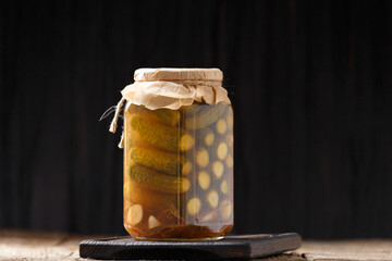 Pickled cucumbers in a jar on a dark background with place for text close-up.