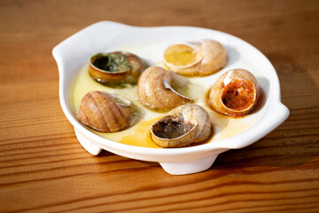 Cooked escargot snails with various sauces on a white dish on a wooden table.