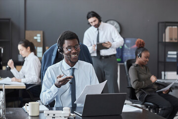 African American broker in headphones talking to customer while sitting at his workplace with laptop