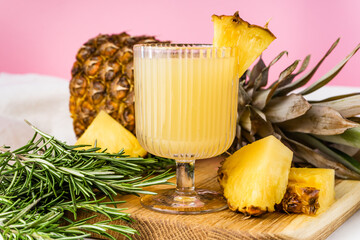 a glass of pineapple juice and a pineapple on wooden tray