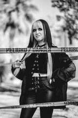 Dangerously stylish: young woman in goth accessories rocks black outfit and poses with funny face behind a danger line in park (in black and white)