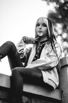 Cozy autumn vibes: beautiful young woman with black and blonde hair in pink jacket and black boots enjoying fall leaves in park (in black and white)