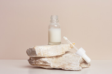 Glass dropper bottle with extract coconut or serum on natural stones, beige color background. Natural Organic Spa Cosmetic trendy concept, minimal style mock up of beauty product packaging