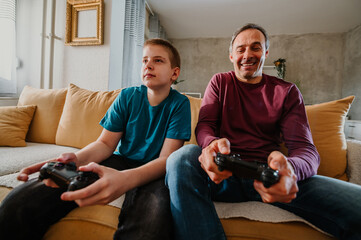 Focused young boy and his father playing video game and enjoying their weekend.