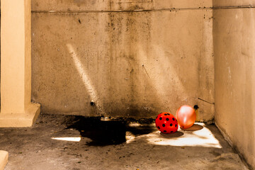 Red with black polka dots and pink balloons on a wet concrete garage floor. Moldy tan walls and rays of sun.